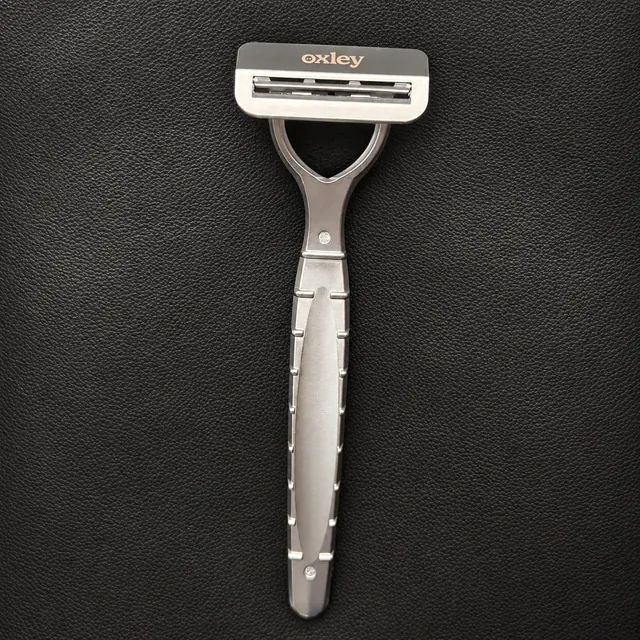 Silver Oxley razor resting on black leather